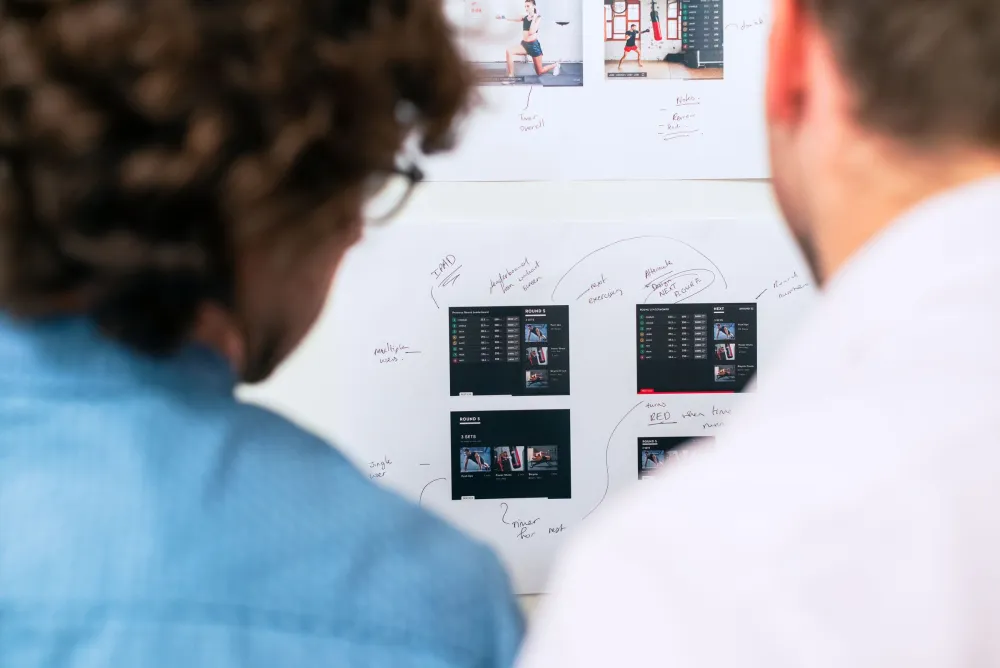 Two colleagues planning a software product in front of a wall of app wireframes